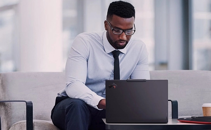 A man working on a Lenovo ThinkPad laptop seated on a modern office sofa.