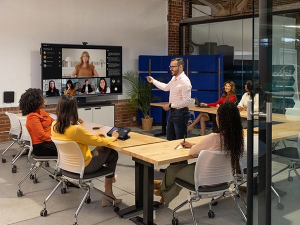 People in a meeting, with one Person using a Lenovo IP Controller, part of Lenovo ThinkSmart Core Full Kit with IP Controller for Teams, with others on the same Teams call shown on a large monitor.