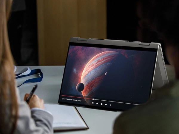 Front, right side view of Lenovo ThinkBook 14 2-in-1 Gen 4 (14” Intel) laptop in tent mode placed on a desk, focusing its display & showing students using it to play a planetary video. 