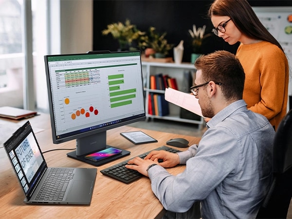 Two people at a desk using a Lenovo laptop and wireless keyboard and mouse to work with data on a Lenovo ThinkCentre Neo 50a Gen 5 24 inch Intel monitor