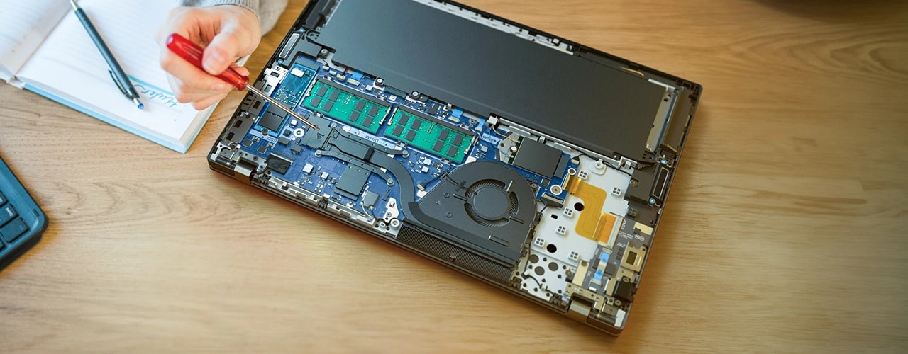 Lenovo ThinkPad T16 Gen 3 (16'' Intel) Notebook – auf einem Schreibtisch, Abdeckung entfernt, um die Komponenten im Inneren zu zeigen, und eine Hand deutet mit einem Schraubenzieher
