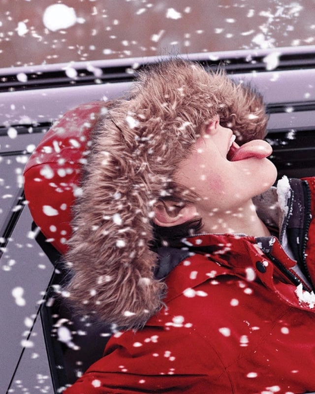 Young boy sticking his head out of a car sticking his tongue out to catch snowflakes