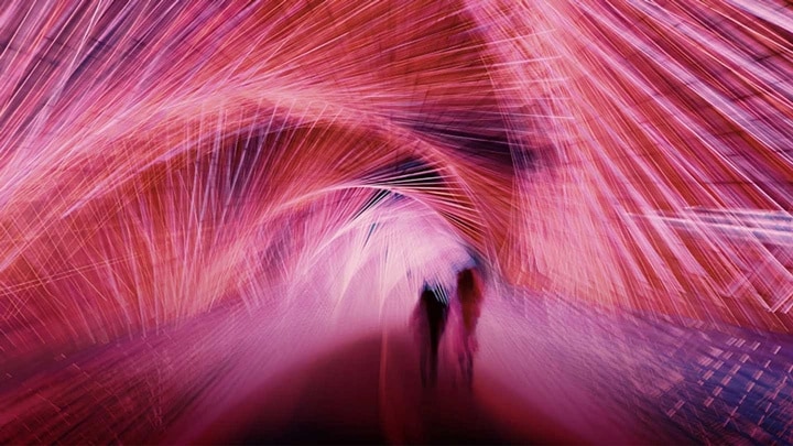 Un abstrait de lumières rouges formant un tunnel que deux personnes traversent