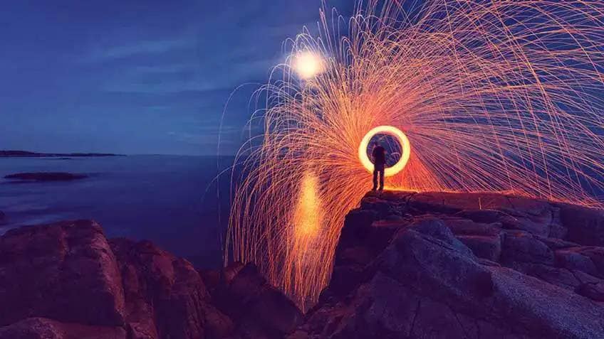 A timelapse of a person waving a sparkler in a circle while standing on a cliff at night 