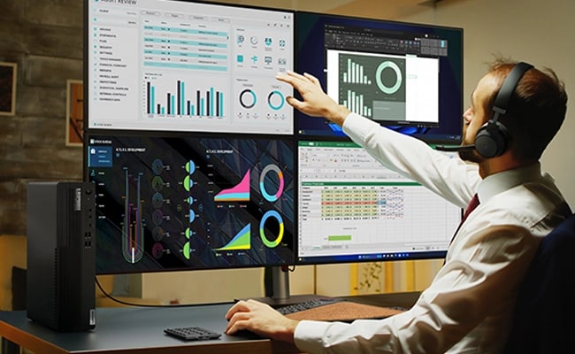 Ein Mann im mittleren Alter sitzt vor vier Monitoren und schaut sich Grafiken und Diagramme an, wobei das Lenovo ThinkCentre 90s Gen 5 im Vordergrund steht.