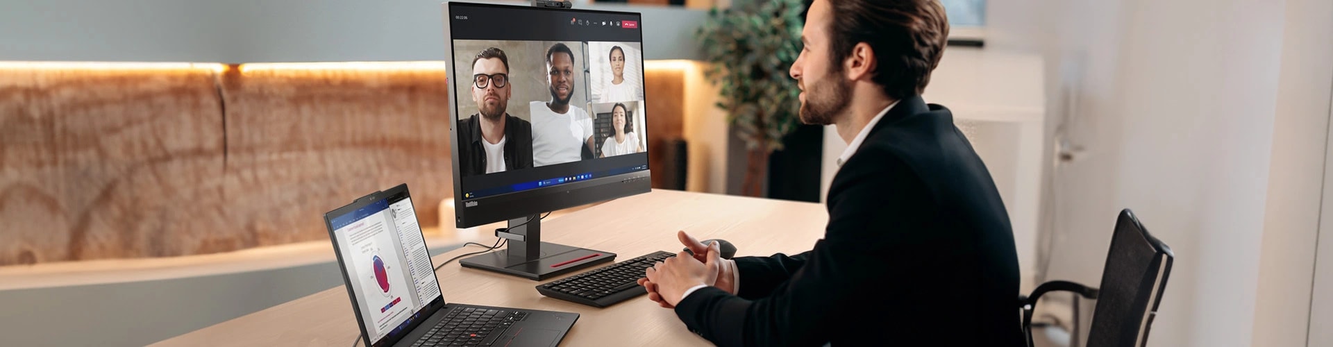 A person having a video conference call on the Lenovo ThinkCentre desktop, connecting it to Lenovo ThinkPad T14 Gen 5 (14” AMD) Eclipse Black laptop with some data-centric documents opened on the laptop.