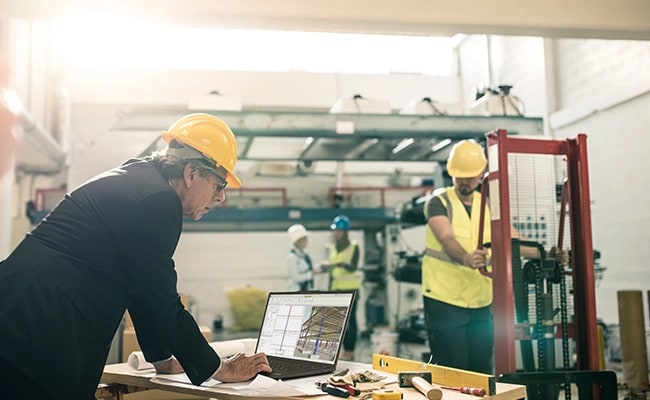 A person working on the Lenovo ThinkPad P16s Gen 3 (16 inch Intel) black laptop placed on a desk in an indoor construction setting with other workers & reviewing some data-centric technical drawings on the laptop.