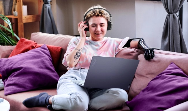 A teen curled up on the couch using her laptop and wearing headphones.