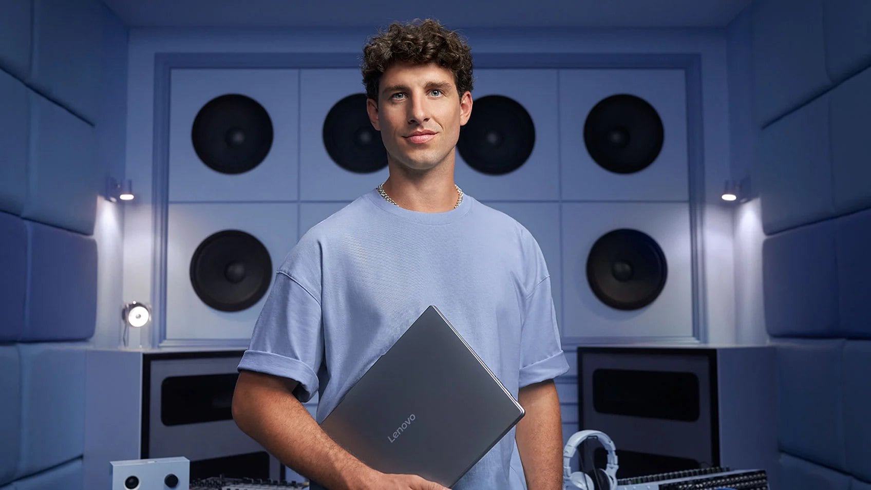 A man holding his laptop and standing in front of a wall of speakers