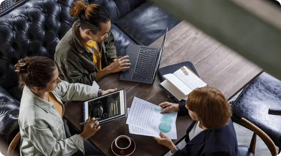 Overhead view of three people sitting at a table, one reviewing documents, one using a Lenovo tablet, and one using a Lenovo laptop.