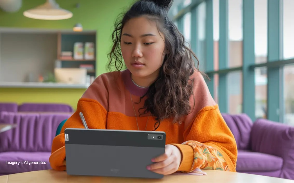 A young woman sitting at a table surrounded by purple couches using a Lenovo tablet on the tabletop.