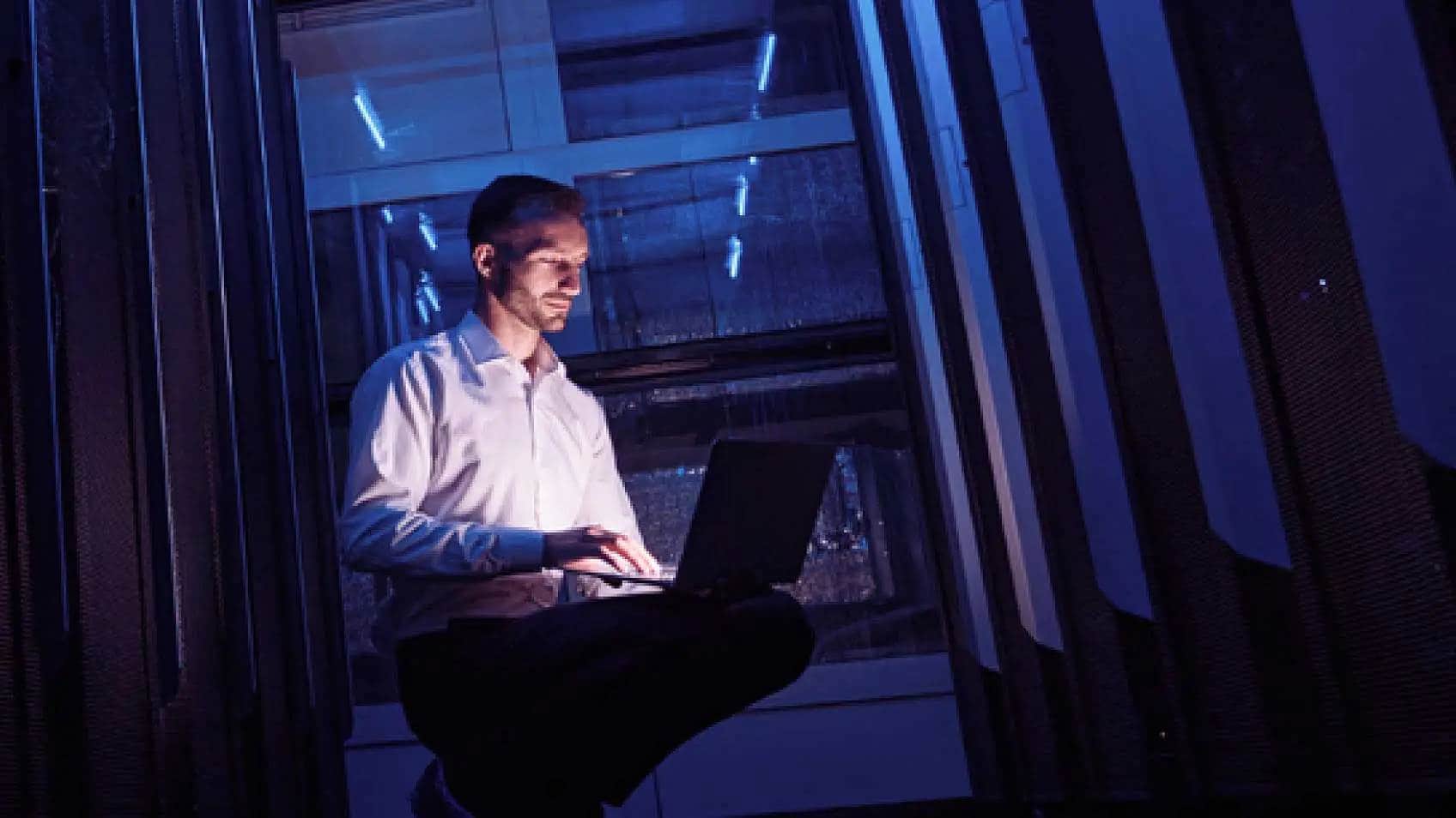 Un homme dans une salle de serveur obscure utilisant un portable.