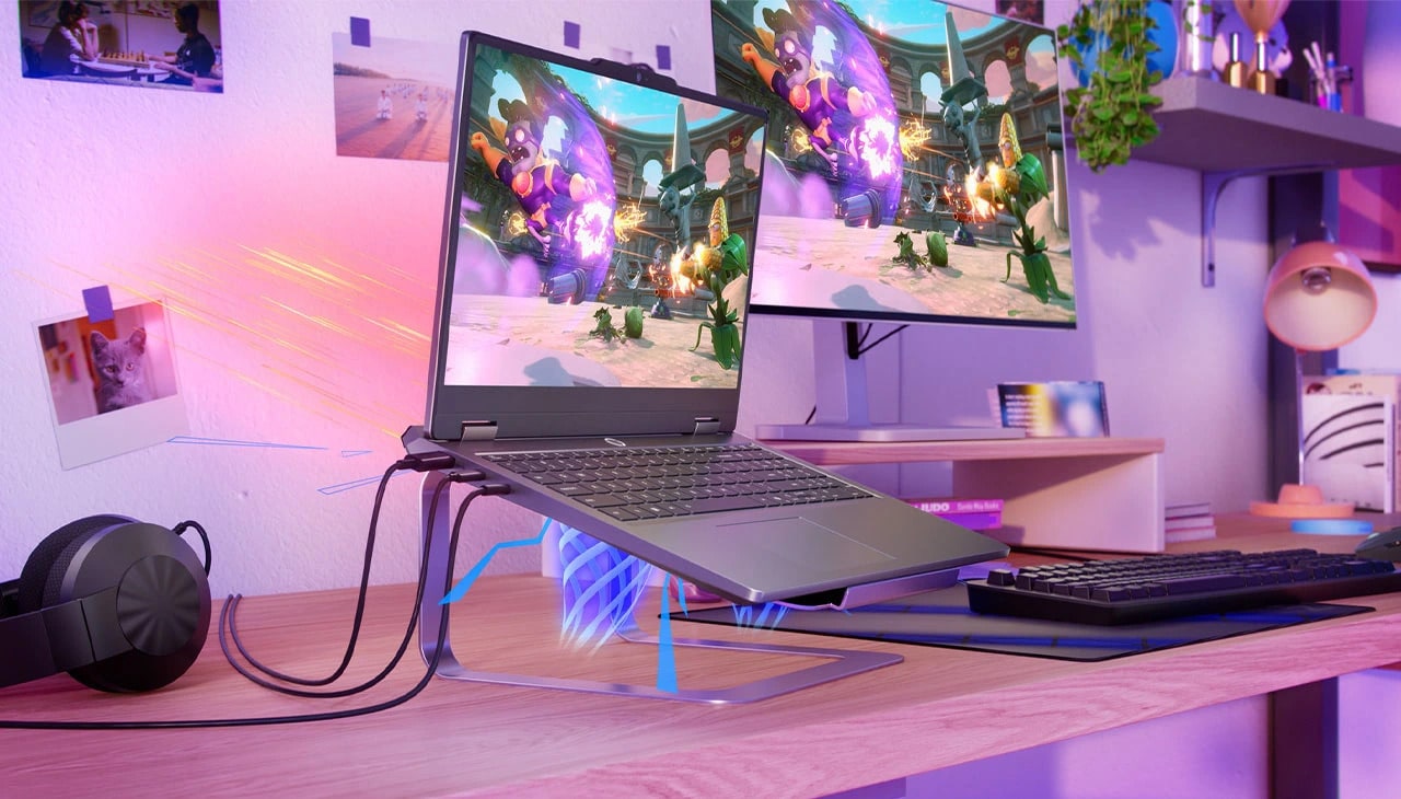 Lenovo LOQ Essential 15IRX11 gaming laptop on a stand on a desk with headset, a keyboard, and a monitor – left-front view, lid open, with a videogame screen on the display.