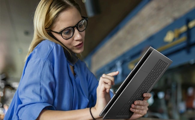 A woman talks on the phone as she looks at a ThinkBook laptop in tablet mode.