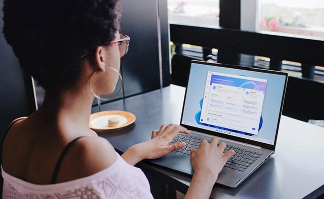 Over-the-shoulder view of a woman sitting at a table, typing on the Lenovo ThinkBook 16 Gen 9 laptop.
