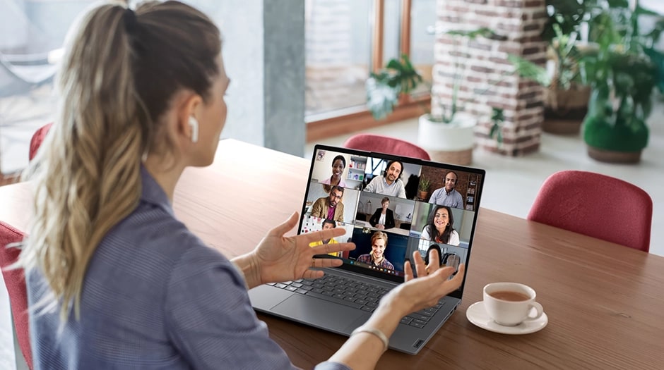 Over-the-shoulder view of a woman on a large video call using a ThinkBook 16 Gen 9 laptop.