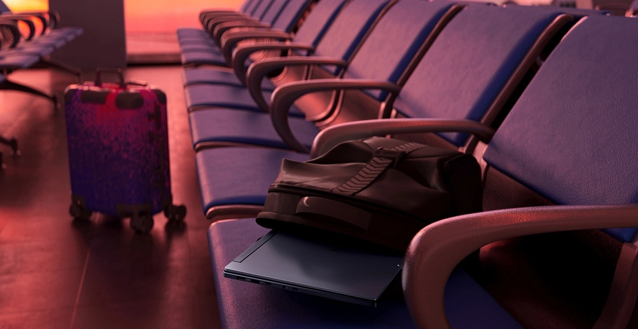 Lenovo Legion laptop tucked under a backpack on airport seats, next to a vibrant patterned suitcase.