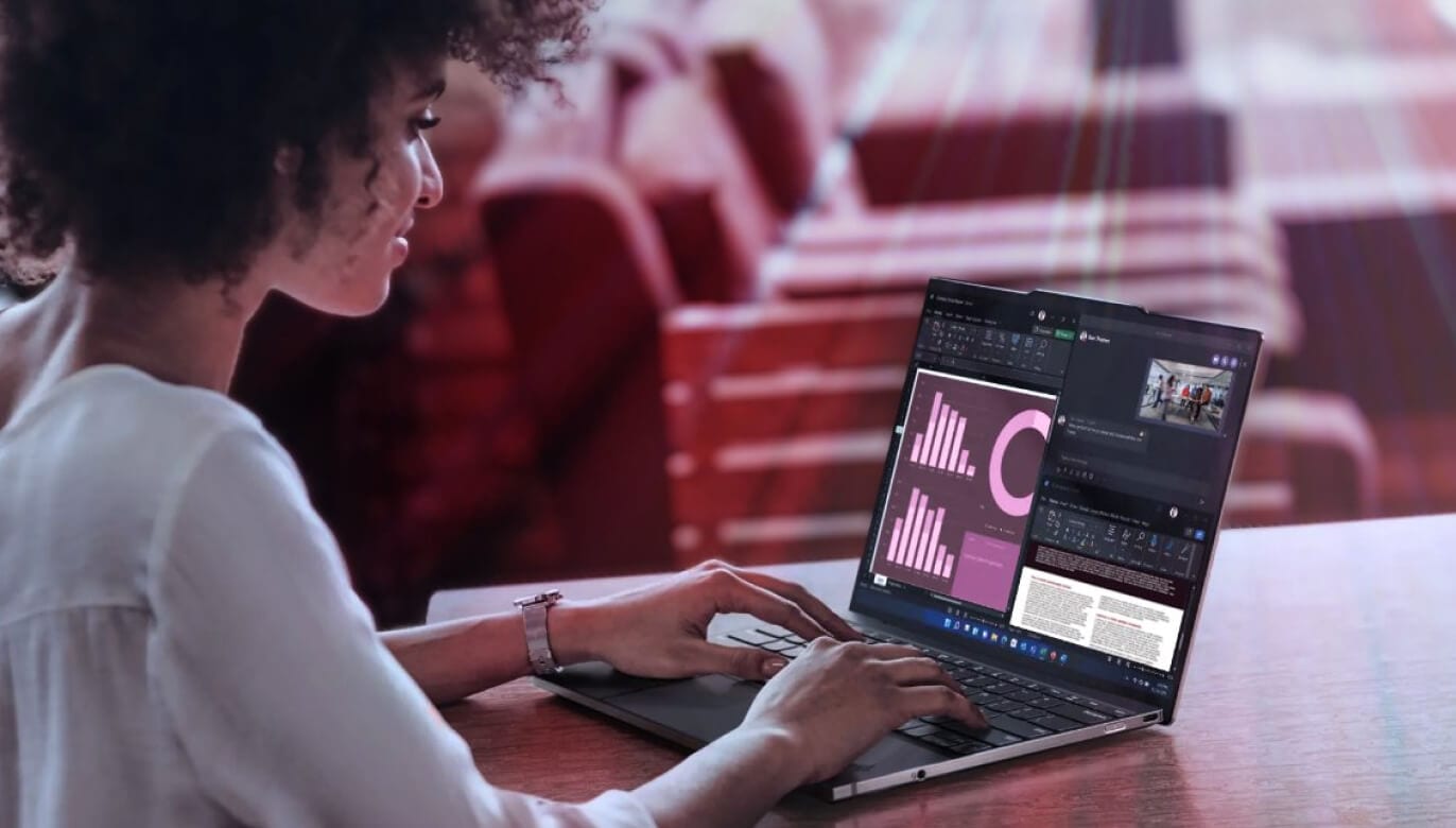 A woman works on a laptop displaying charts and graphs, seated in a casual setting with a red-tinted background.