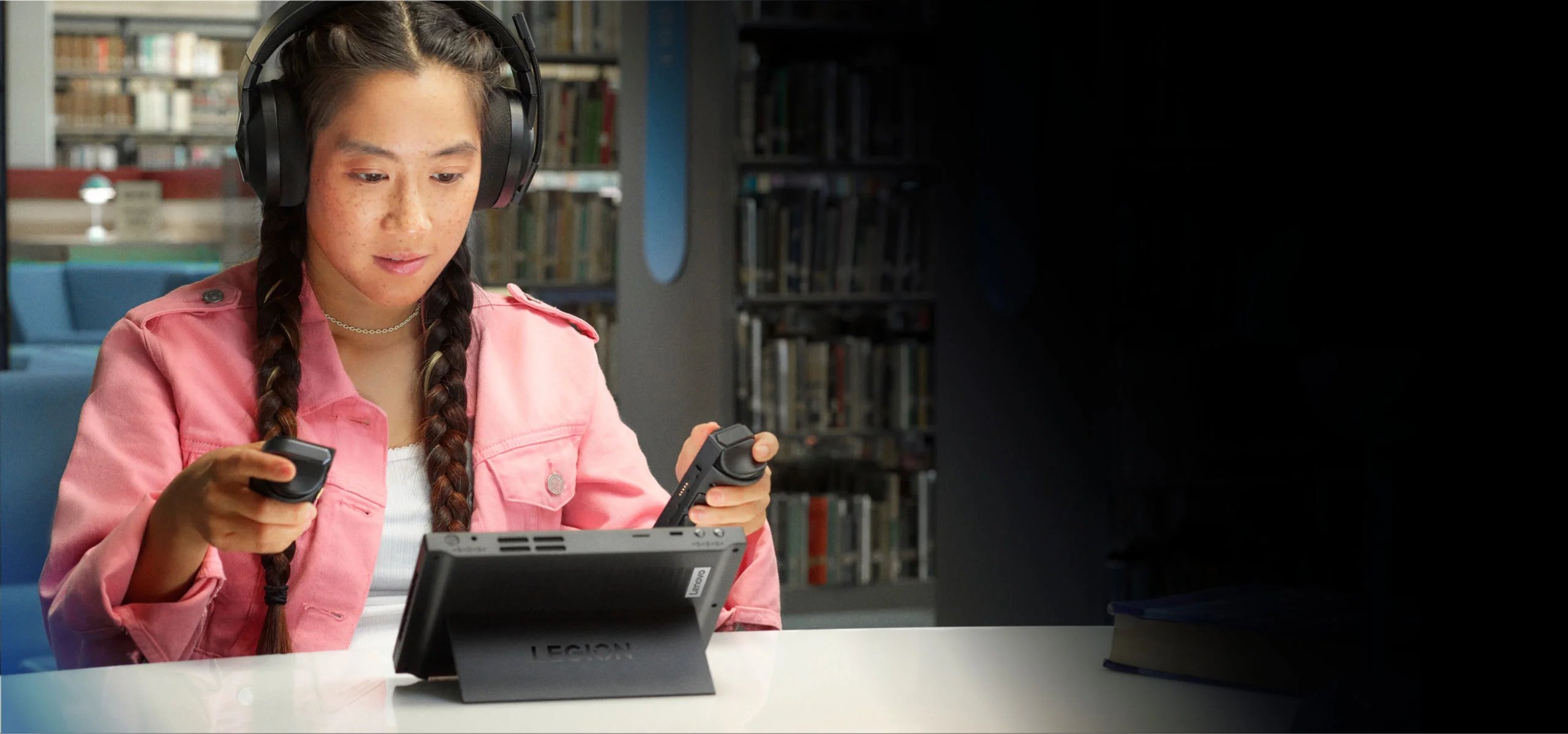 A young lady holding the Lenovo Legion Go controllers with the Legion Go system sitting in front of her 