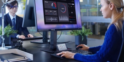 Une femme travaillant au bureau visionnant un graphique sur un moniteur Lenovo. En face d’elle, un homme travaille également sur son bureau,