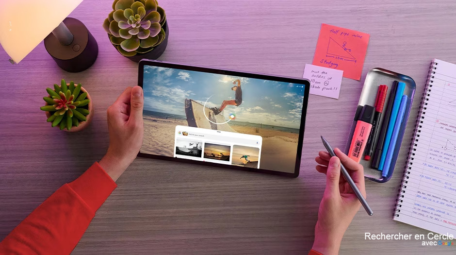 Two hands hold a Lenovo Idea Tab Pro tablet in Luna Grey and a Lenovo Tab Pen Plus atop a desk, having just initiated Circle to Search with Google on the tablet