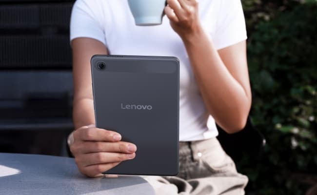 טאבלט 8.7 Tab One מבית Lenovo A person smiles as they hold up and use a Lenovo Tab One tablet, with two tall buildings in the background.
