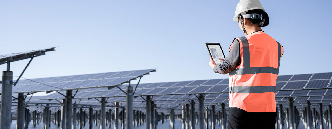 A worker in a hard hat monitors solar panels in a field with a Lenovo ThinkTab X11 tablet.
