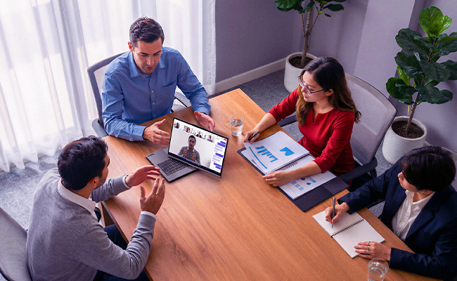 Professionals around a table use a laptop for video conferencing, showcasing seamless collaboration with the Lenovo ThinkBook Plus Gen 7 Auto Twist (14″ Intel) laptop.