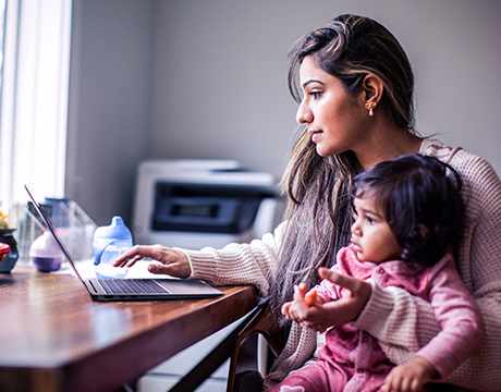 A woman works on the Lenovo ThinkPad P14s Gen 7 (14" AMD) mobile workstation holding a child in her lap, showcasing flexibility with the laptop.