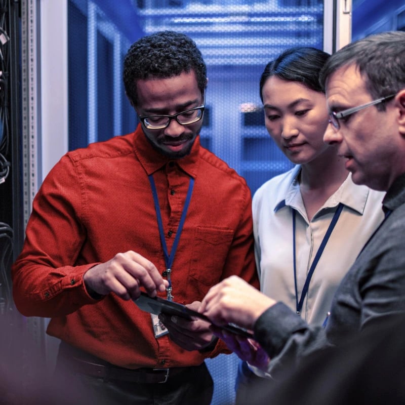 Three people standing in a data center looking at information on a tablet device.