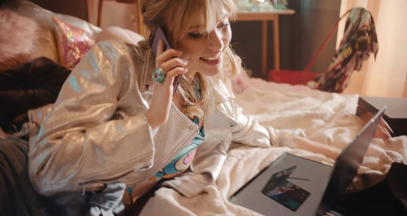 Une jeune femme recevant une assistance technique au téléphone alors qu’elle utilise son PC dans sa chambre.