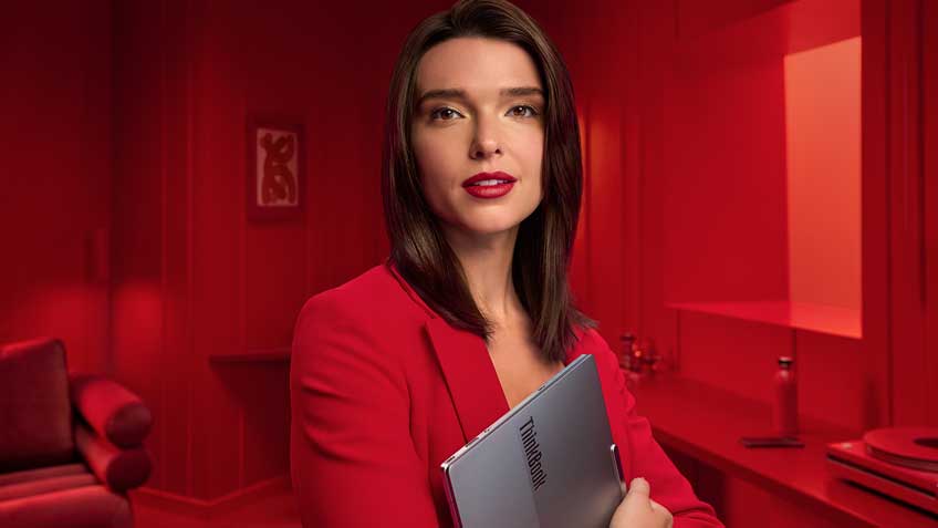 A woman dressed in red in a red room holding her ThinkBook to her chest