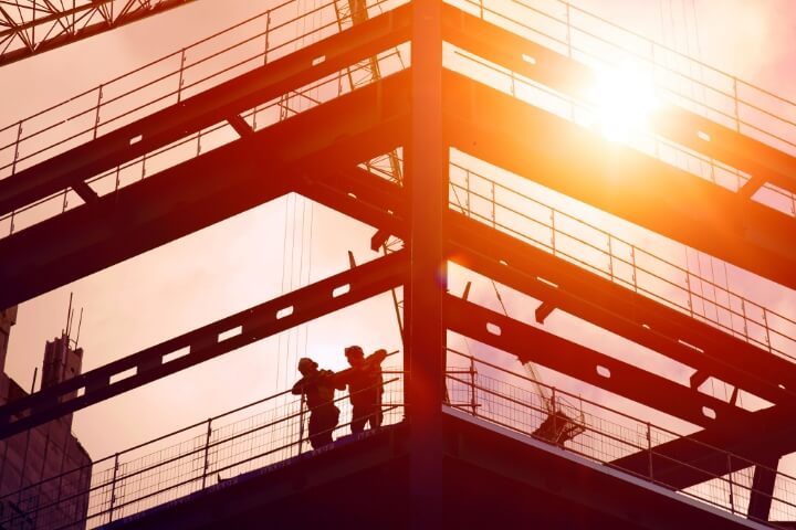 Image of a construction site with two construction workers looking down from a multifloored building.