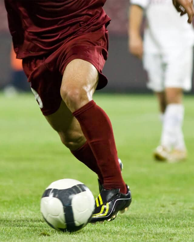 Image of a soccer player kicking a soccer ball on the pitch.