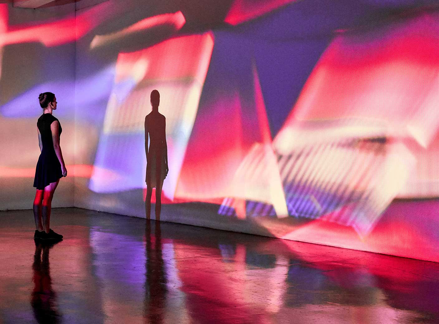 壁の前に立つ女性。壁にはカラフルな光が投影されている。