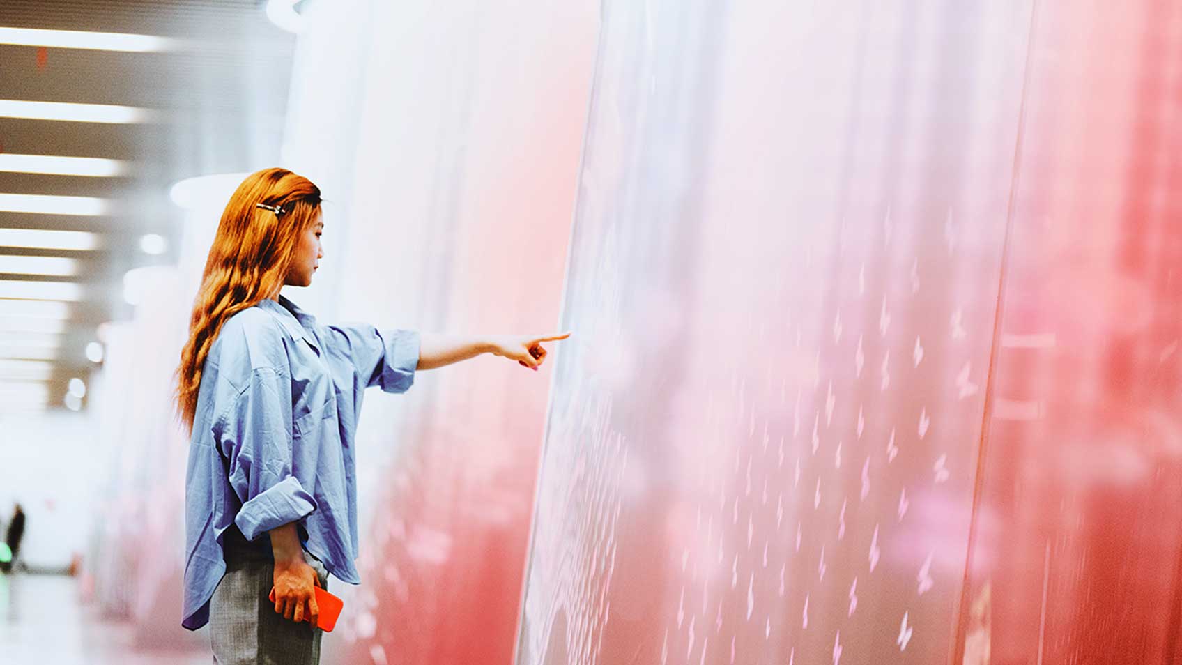 Woman holding her arm out pointing at a very large pink screen.