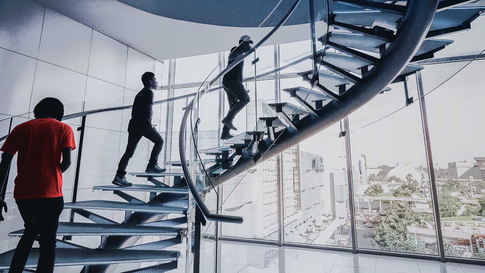 Trois personnes montant un escalier moderne en spirale.
