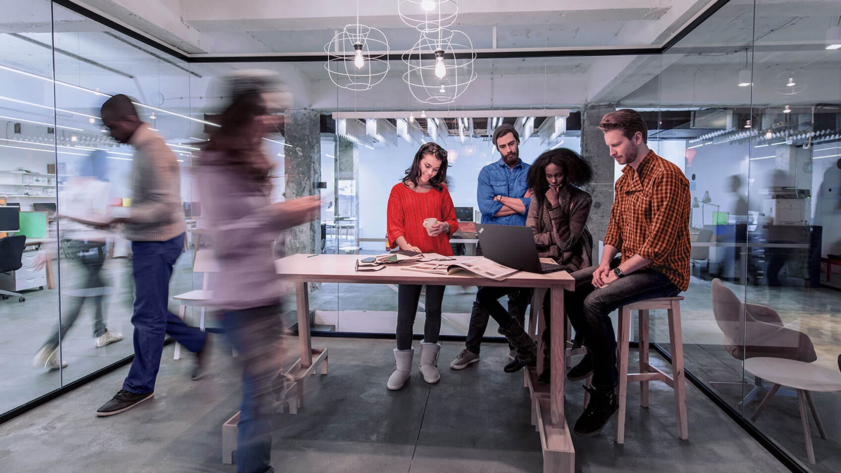 Colleagues gathered around a tall conference table in a meeting room with all glass walls