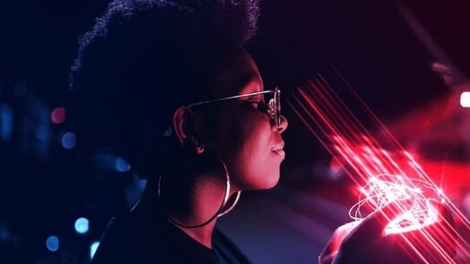 A woman smiles while holding glowing red lights in the dark