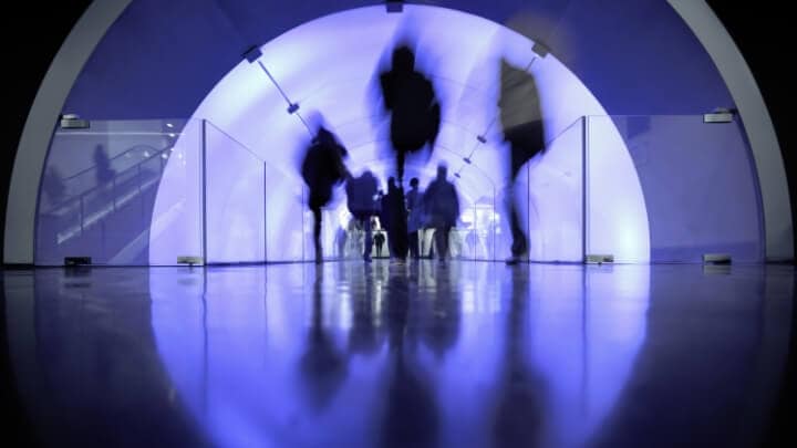 An image of motion-blurred silhouettes of people walking into an office.