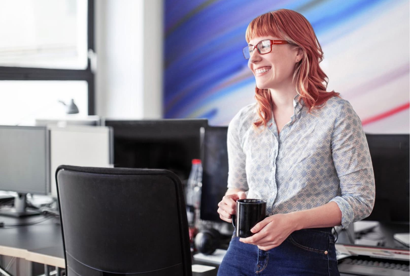 Une femme au bureau, accoudée contre la table de conférence et tenant une tasse de café