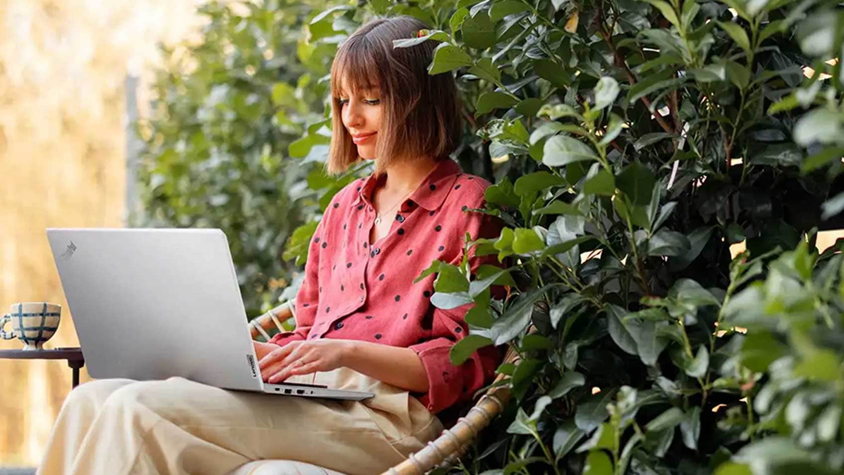 A woman working on her laptop outside seated in front of a hedge