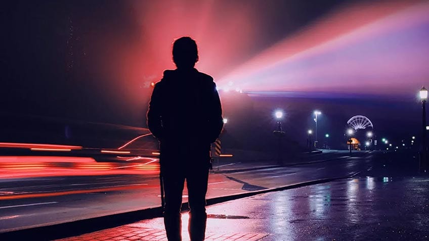 A person silhouetted at night with a blur of city lights behind him