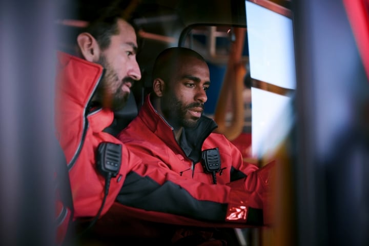 Two emergency responders in red jackets inside a vehicle, focused on their task.