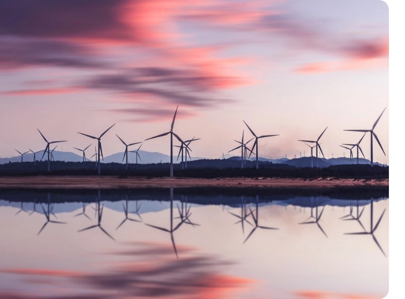 A field of wind turbines behind water, in sunset