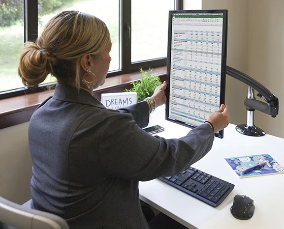 Person with vertical monitor displaying a spreadsheet