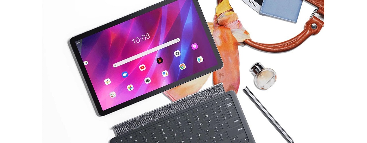 Tableta Lenovo Tab P11 Plus: vista frontal con pantalla de inicio y varios íconos de aplicaciones en la pantalla, además de teclado y bolígrafo opcionales, todo sobre el bolso y la bufanda, con varios artículos personales desparramados