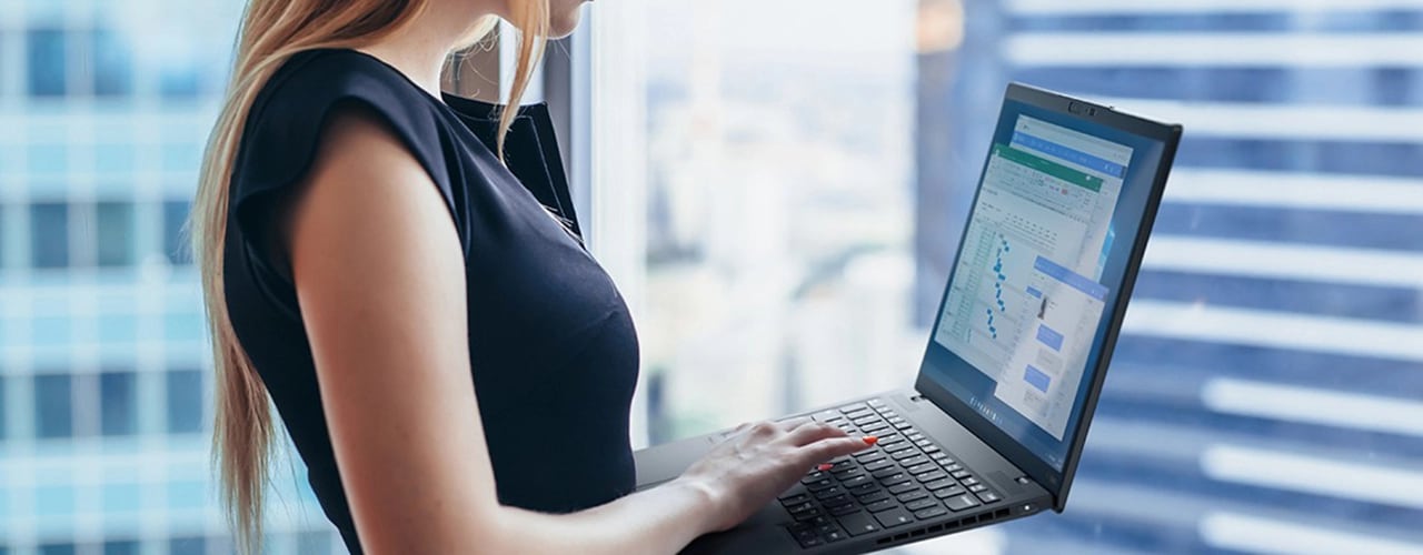 Une femme tient le Lenovo ThinkPad X1 Nano, tout en tapant sur le clavier, avec divers graphiques à l’écran.