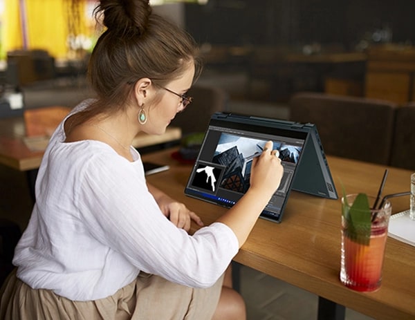 A woman using the Lenovo ThinkBook 14s Yoga Gen 3 2-in-1 in tent mode with the included smart pen.
