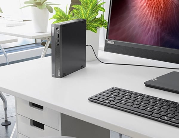 Lenovo ThinkCentre Neo 50q Gen 4 (Intel) Thin Client, Nahaufnahme von der Seite, aufrecht auf einem Büroschreibtisch stehend, neben einem Monitor und einer Tastatur (separat erhältlich)